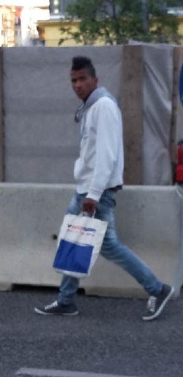 Ein junger Mann geht mit einer Einkaufstasche von Intersport die Straße entlang.