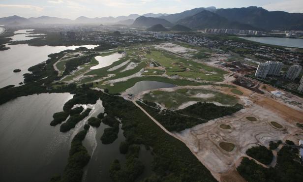Luftaufnahme eines Golfplatzes in Küstennähe mit Bergen im Hintergrund.