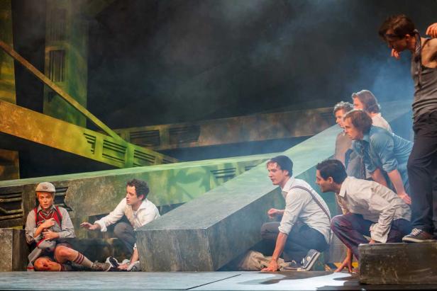 Auf einer Bühne kauern mehrere Schauspieler vor einer abstrakten, grünen Kulisse.