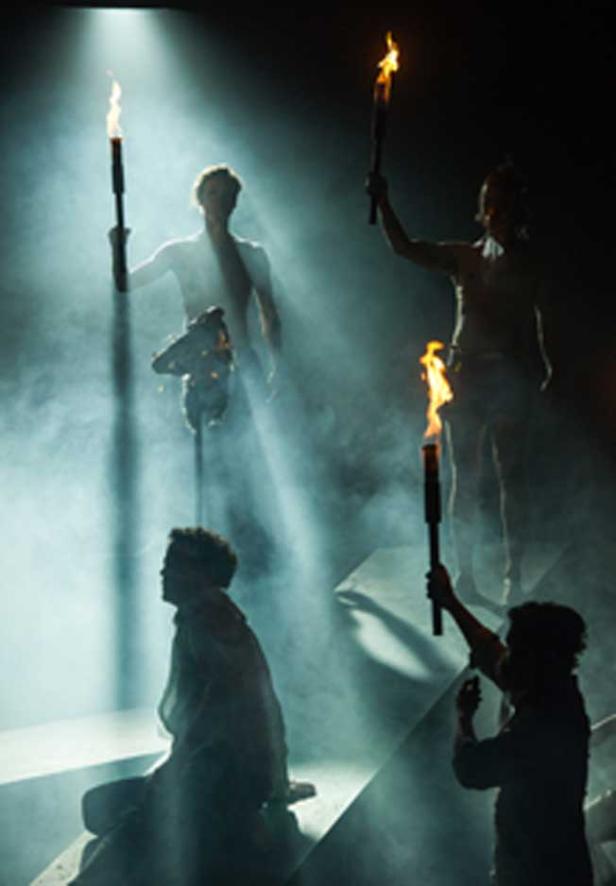 Mehrere Personen mit Fackeln stehen auf einer Bühne im Nebel.