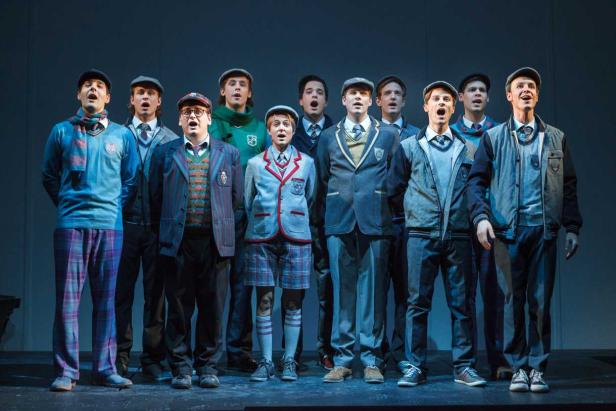Eine Gruppe junger Männer in Schuluniformen singt gemeinsam auf einer Bühne.