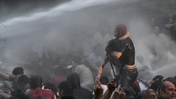 Ein Mann trägt eine andere Person durch eine Menschenmenge, während sie von einem Wasserwerfer getroffen werden.