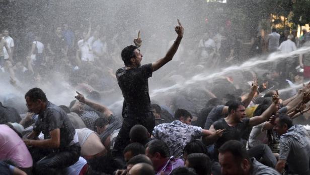 Eine Menschenmenge wird mit Wasserwerfern bespritzt, einige zeigen den Mittelfinger.