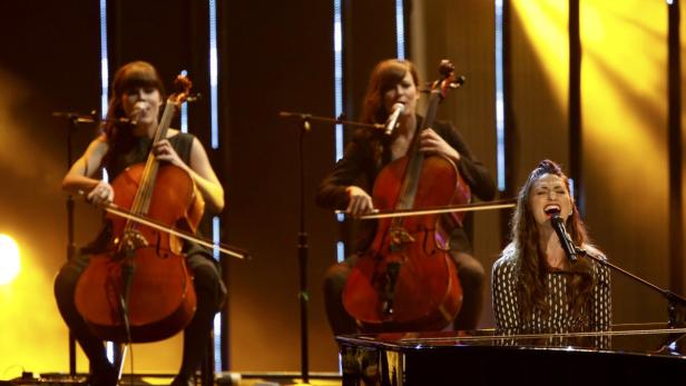 Eine Sängerin spielt Klavier, begleitet von zwei Cellistinnen auf einer Bühne.