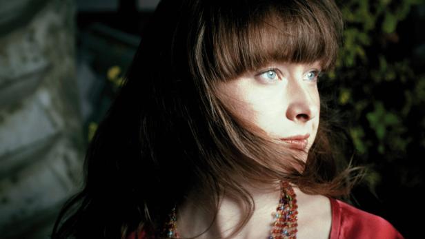 Porträt einer Frau mit braunen Haaren und einer bunten Halskette.