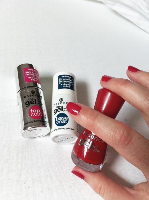 Eine Hand hält einen roten Nagellack von Essence, daneben Base- und Topcoat der gleichen Marke.