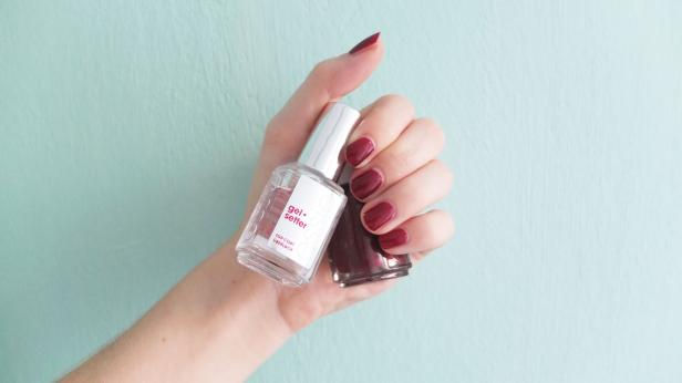 Eine Hand hält Nagellack und Überlack der Marke Essie mit rot lackierten Nägeln.