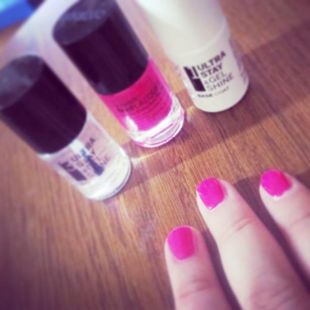 Eine Hand mit pinkfarben lackierten Nägeln und drei Nagellackflaschen.