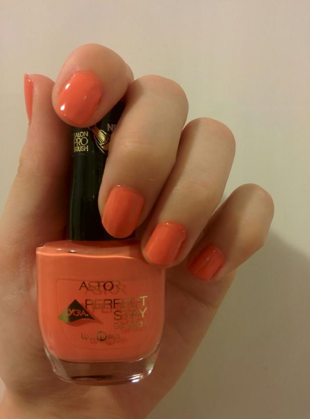 Eine Hand hält eine Flasche orangefarbenen Nagellack der Marke Astor Perfect Stay.