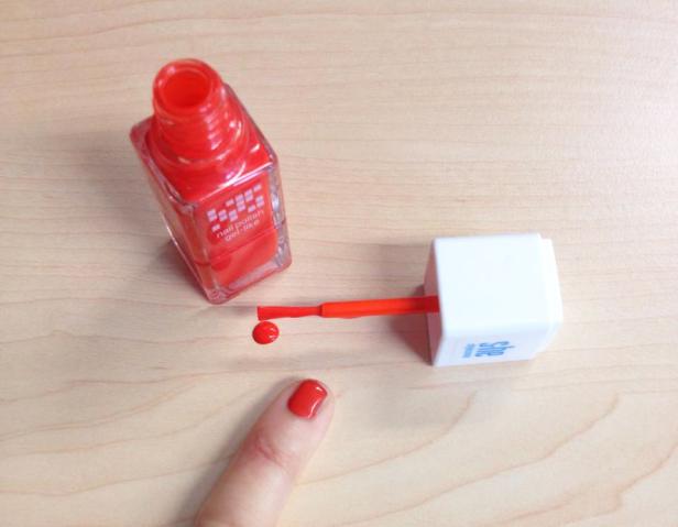 Eine Flasche roter Nagellack, ein Pinsel und ein bemalter Fingernagel auf einem Tisch.