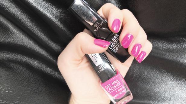 Eine Hand hält Nagellack und Überlack der Marke Isadora in Pink vor einem schwarzen Hintergrund.