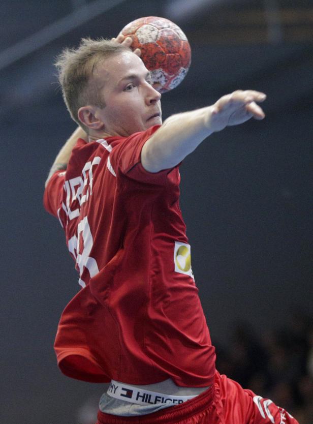 Ein Handballspieler in rotem Trikot wirft einen Ball.