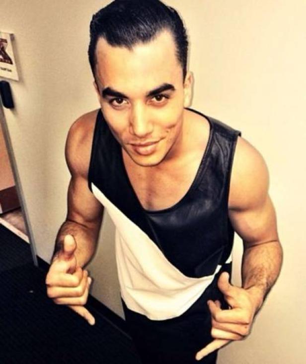 Ein Mann mit gegelten Haaren posiert in einem schwarz-weißen Tanktop.