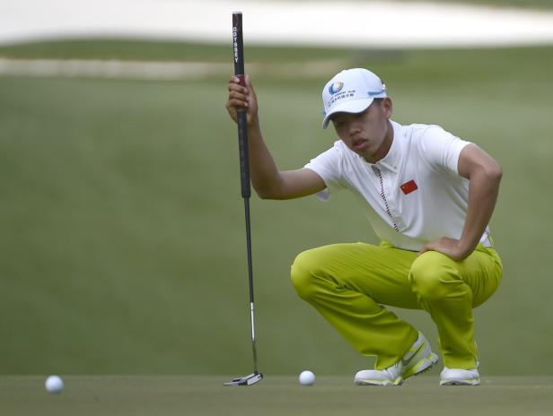 Ein chinesischer Golfer kauert auf dem Grün und zielt mit seinem Putter.
