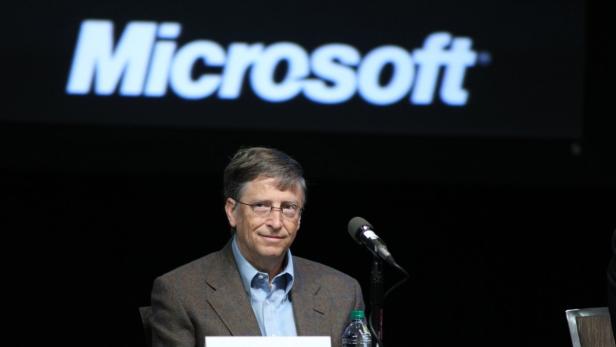 Bill Gates sitzt vor einem Mikrofon mit dem Microsoft-Logo im Hintergrund.