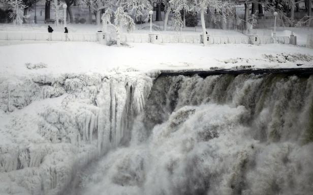 Ein gefrorener Wasserfall mit zwei Personen im Hintergrund.