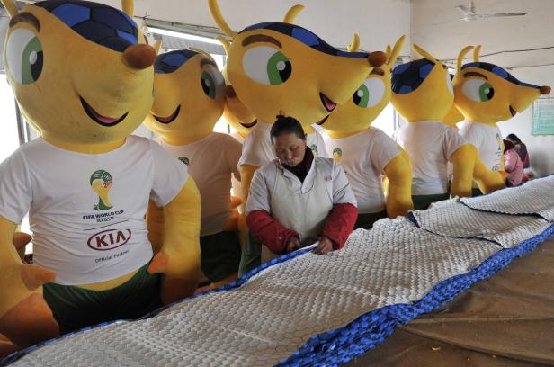 Eine Frau arbeitet an einer Matte vor einer Reihe von Fuleco-Maskottchen der FIFA Fussball-Weltmeisterschaft 2014.