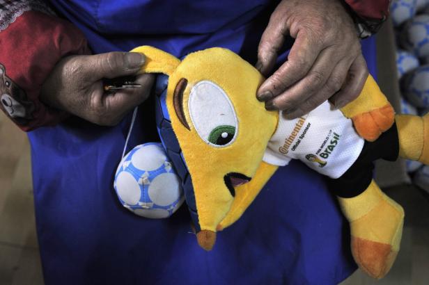 Eine Person flickt ein Plüschtier-Gürteltier, das ein Trikot der FIFA Fussball-Weltmeisterschaft Brasilien trägt.