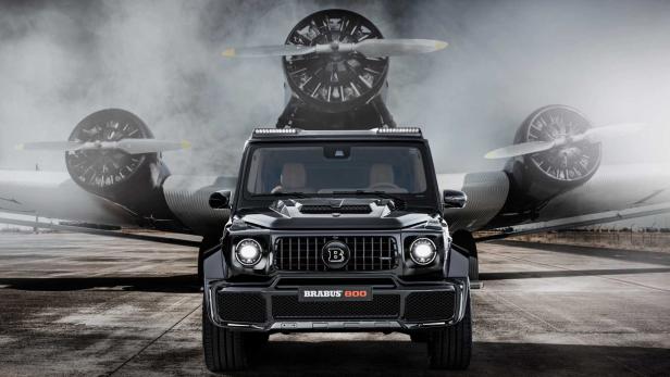 Ein schwarzer Brabus 800 steht vor einem historischen Flugzeug.