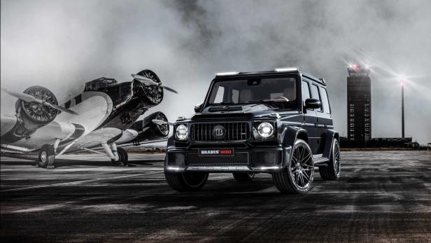 Ein schwarzer Brabus 800 steht vor einem alten Flugzeug auf einem Flugfeld.