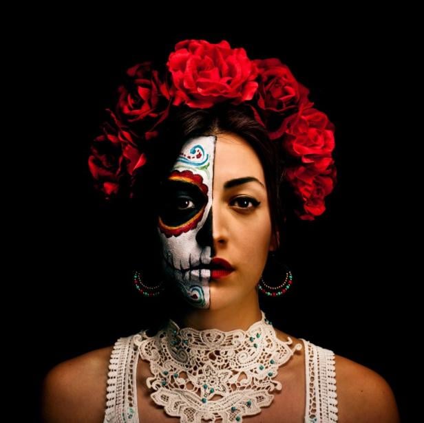 Eine Frau mit rotem Rosenkranz und Gesichtsbemalung im Stil des „Dia de los Muertos“.