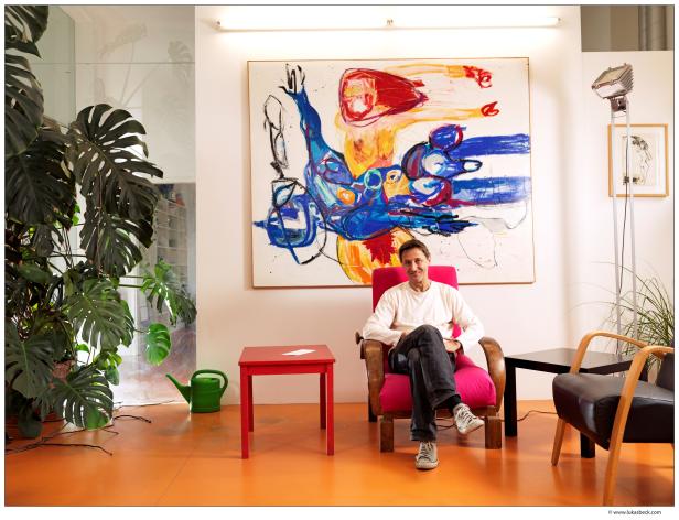 Ein Mann sitzt in einem Sessel vor einem farbenfrohen Gemälde.