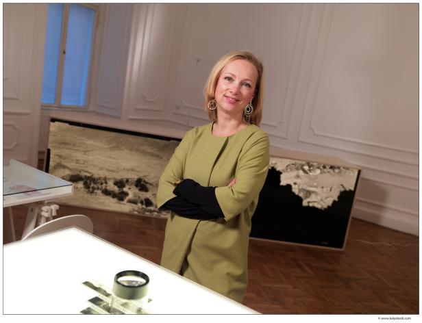 Eine blonde Frau steht mit verschränkten Armen in einem Ausstellungsraum.