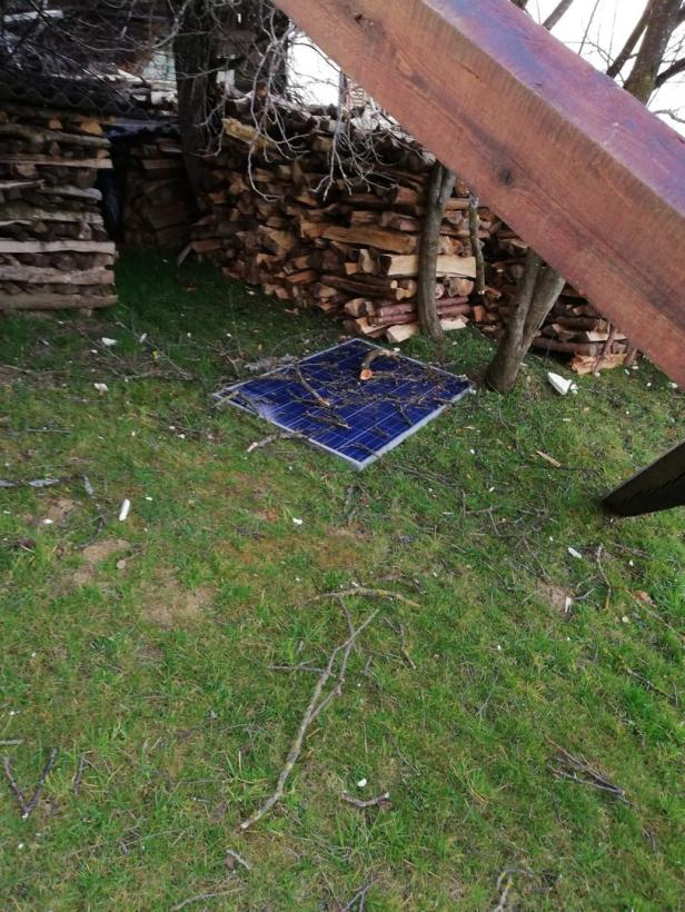 Ein Solarpanel liegt auf einer Wiese neben einem Stapel Holz.