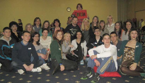 Eine Gruppe junger Menschen sitzt auf dem Boden, einige halten ein Schild mit der Aufschrift „Serbia“.