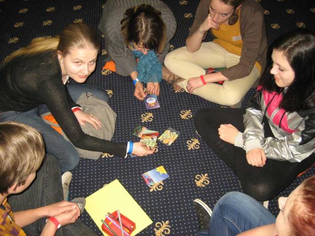 Eine Gruppe junger Leute sitzt auf dem Boden und spielt Karten.