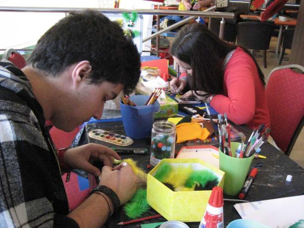 Zwei Personen basteln an einem Tisch mit Federn und Farben.