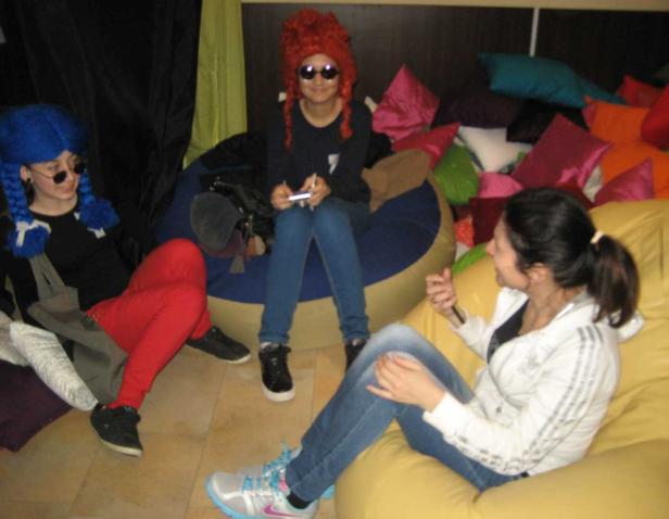 Drei Frauen sitzen auf Sitzsäcken, zwei davon mit bunten Perücken und Sonnenbrillen.