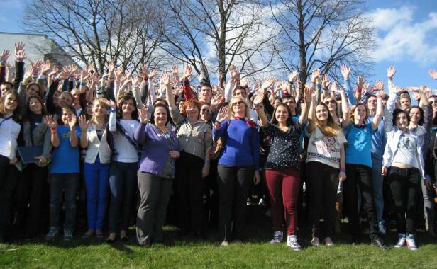 Eine große Gruppe von Menschen winkt mit erhobenen Händen in die Kamera.