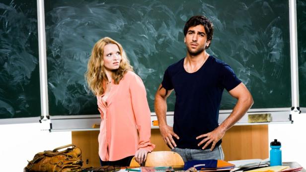 Eine Frau und ein Mann stehen vor einer Tafel in einem Klassenzimmer.