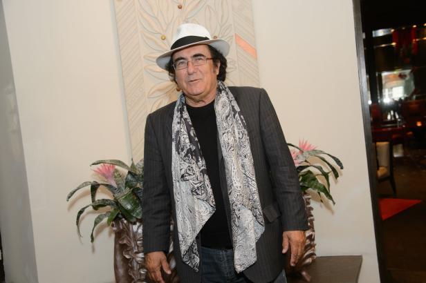 Al Bano Carrisi mit Hut und Schal vor einer Wand mit Dekoration.