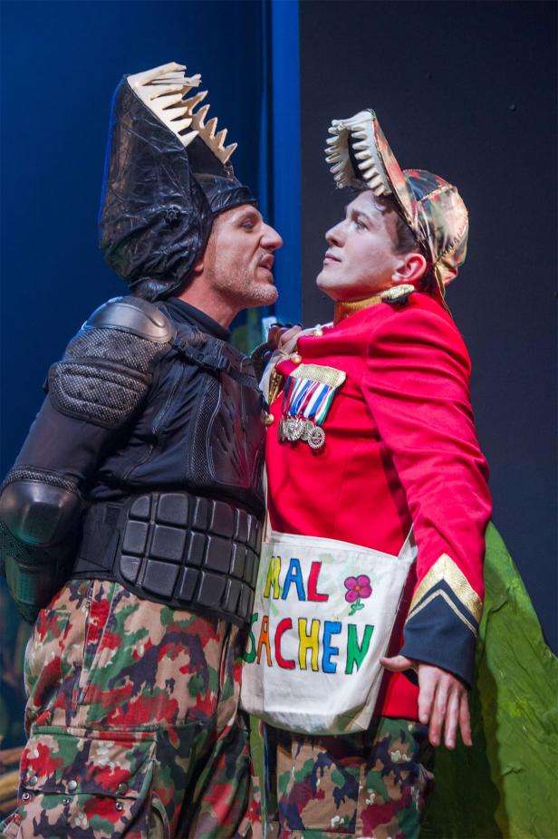 Dinosaurier, Das Musical Zwei Männer in Kostümen stehen sich auf einer Bühne gegenüber.