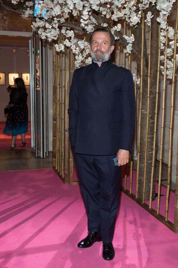 Ein Mann in einem dunklen Anzug steht vor einer Dekoration aus Bambus und Kirschblüten.