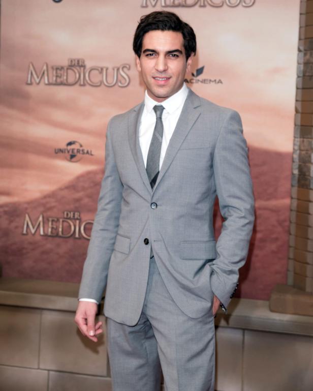 Elyas M'Barek posiert vor einem Plakat für den Film „Der Medicus“.