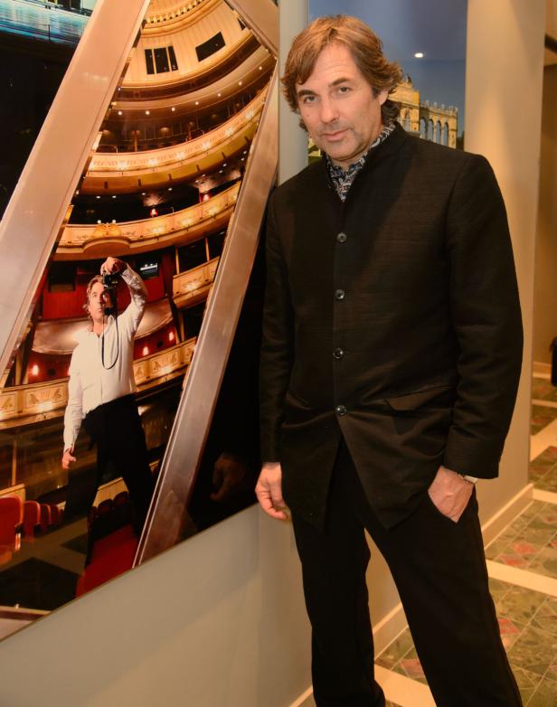 Ein Mann posiert neben einem großen Foto des Inneren eines Opernhauses.