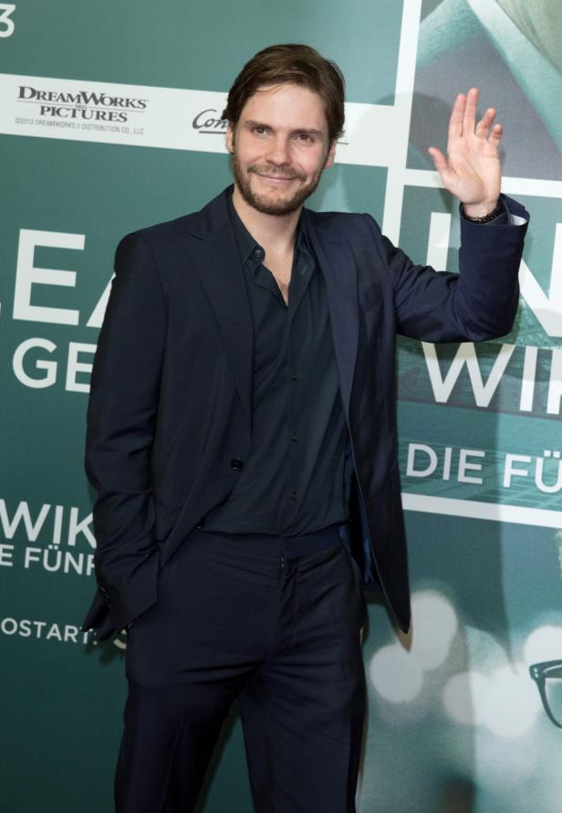 Daniel Brühl posiert auf einer Filmpremiere und winkt in die Kamera.