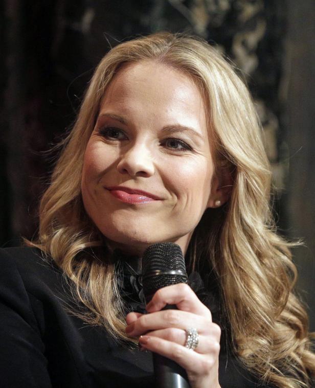 Eine blonde Frau hält ein Mikrofon und lächelt.