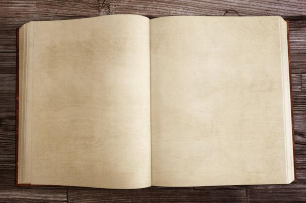 Ein aufgeschlagenes Buch mit leeren, cremefarbenen Seiten liegt auf einem Holztisch.