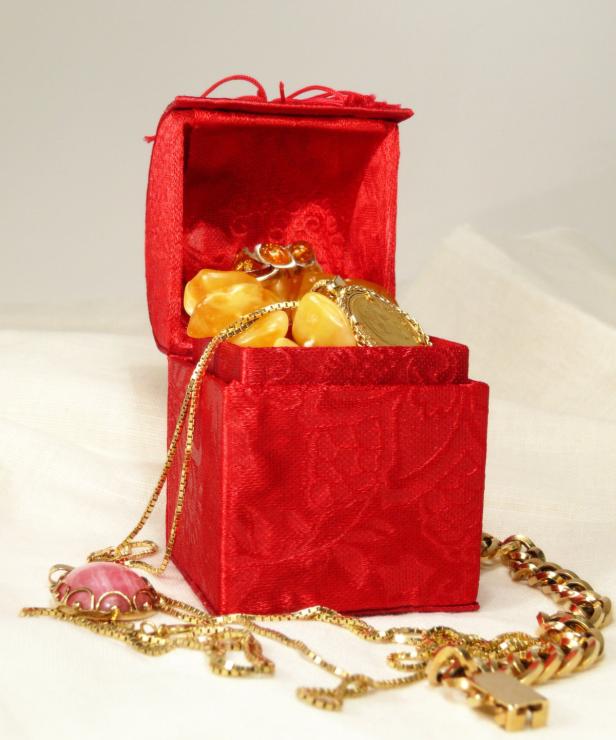 Eine rote Schmuckschatulle ist mit goldenen Halsketten und Bernsteinschmuck gefüllt.