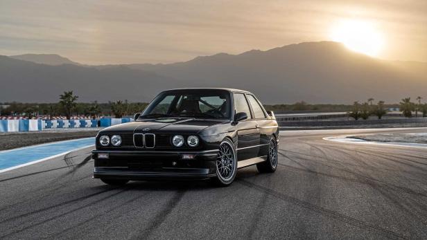 Ein schwarzer BMW E30 steht auf einer Rennstrecke vor einer Bergkulisse.