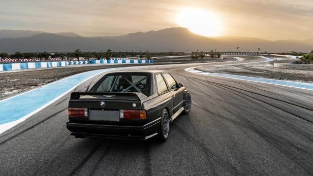 Ein schwarzer BMW E30 auf einer Rennstrecke bei Sonnenuntergang.
