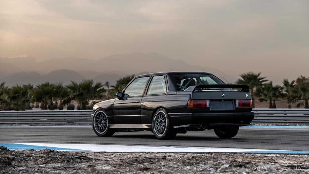 Ein schwarzer BMW E30 mit Heckspoiler auf einer Rennstrecke.