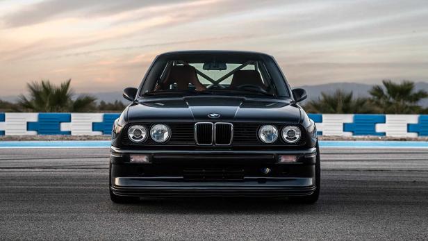 Ein schwarzer BMW E30 steht auf einer Rennstrecke.