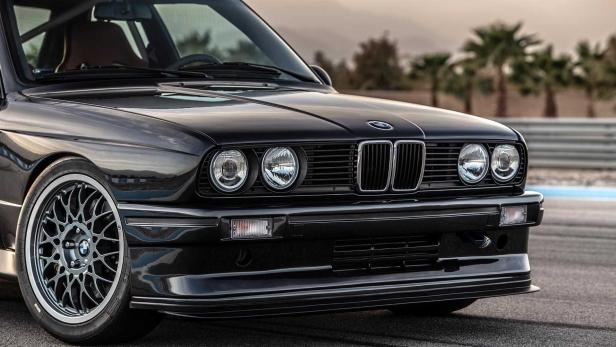 Detailansicht der Frontpartie eines schwarzen BMW E30 mit Scheinwerfern und Kühlergrill.