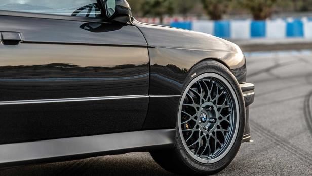 Detailansicht eines schwarzen BMW E30 mit speziellen Felgen auf einer Rennstrecke.