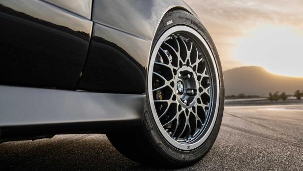 Nahaufnahme eines schwarzen BMW-Autos mit einer silbernen Felge vor einer Bergkulisse.